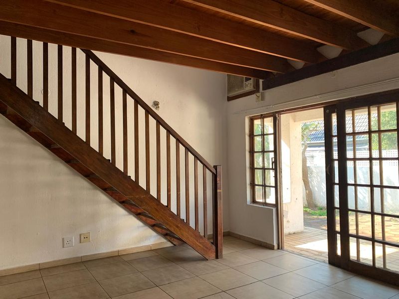 Open plan living area featuring exposed wooden ceiling beams, a wooden staircase, tiled flooring, and direct access to an outdoor patio through sliding doors.
