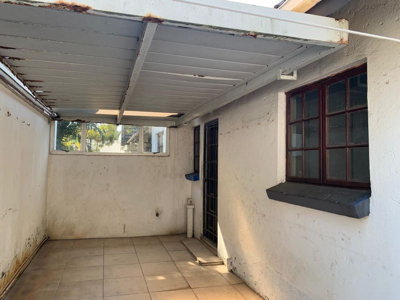 A covered outdoor patio area featuring tiled flooring, a metal roof structure, and security access, requiring maintenance and cosmetic updates.