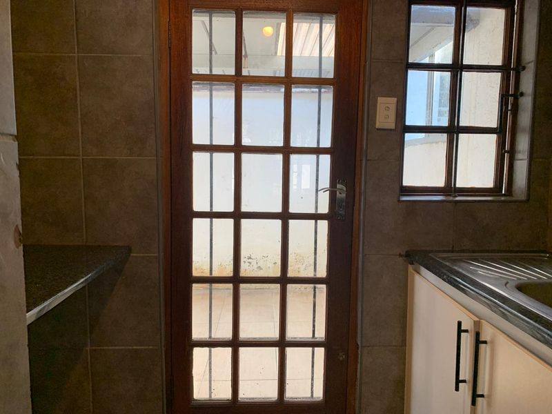 A functional scullery area featuring granite countertops, a stainless steel sink, and a timber-framed glass door leading to an outdoor space.