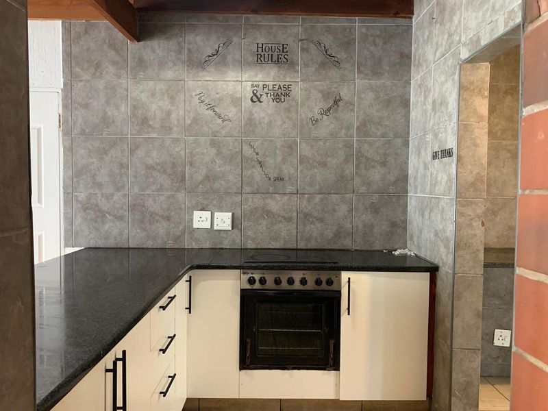 A functional kitchen featuring white cabinetry, dark granite countertops, a built-in oven, and a tiled splashback with decorative wall decals.