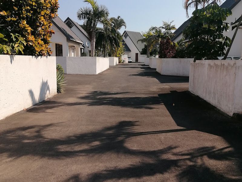 A view of the complex driveway leading towards the townhouse units, featuring paved surfaces and established boundary walls.