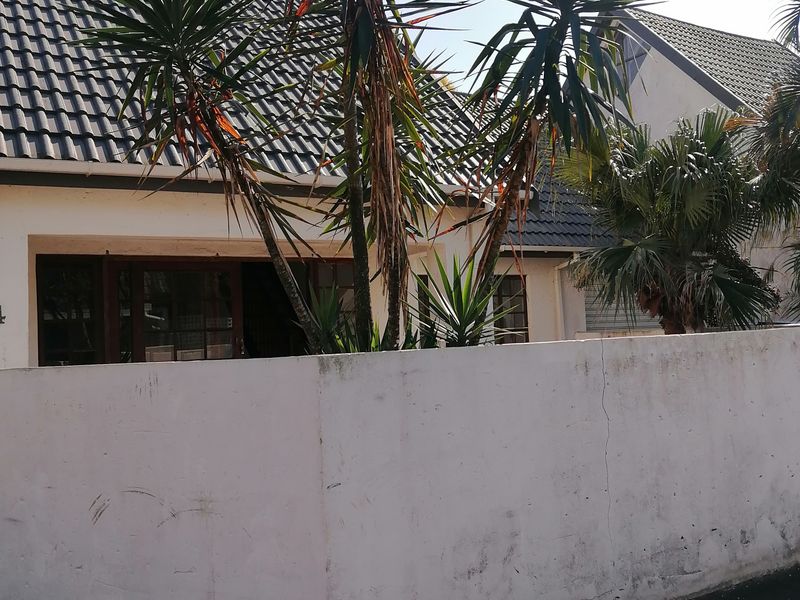 Front exterior view of the townhouse featuring a tiled roof, sliding door access, and a boundary wall requiring maintenance.