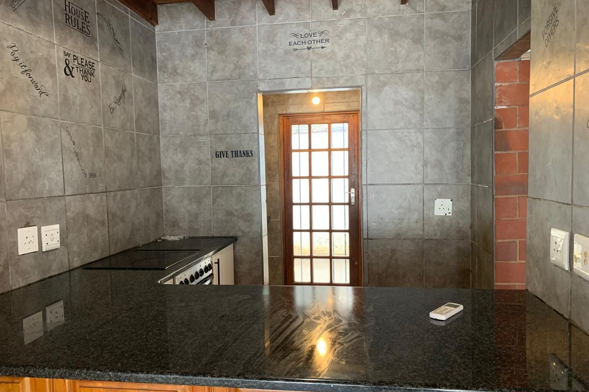 Kitchen area featuring granite countertops, built-in stove, and exposed timber ceiling beams, leading to a timber-framed glass door.