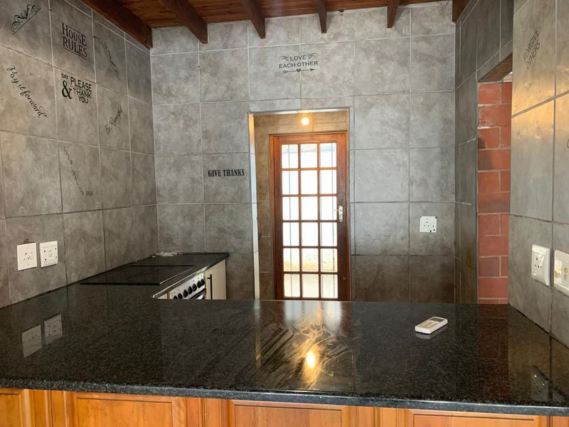 Kitchen area featuring granite countertops, built-in stove, and exposed timber ceiling beams, leading to a timber-framed glass door.