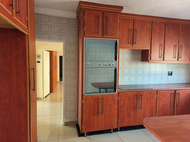 A functional kitchen featuring dated wood-finish cabinetry, built-in oven, electric hob, and tiled flooring, offering potential for a modern renovation.