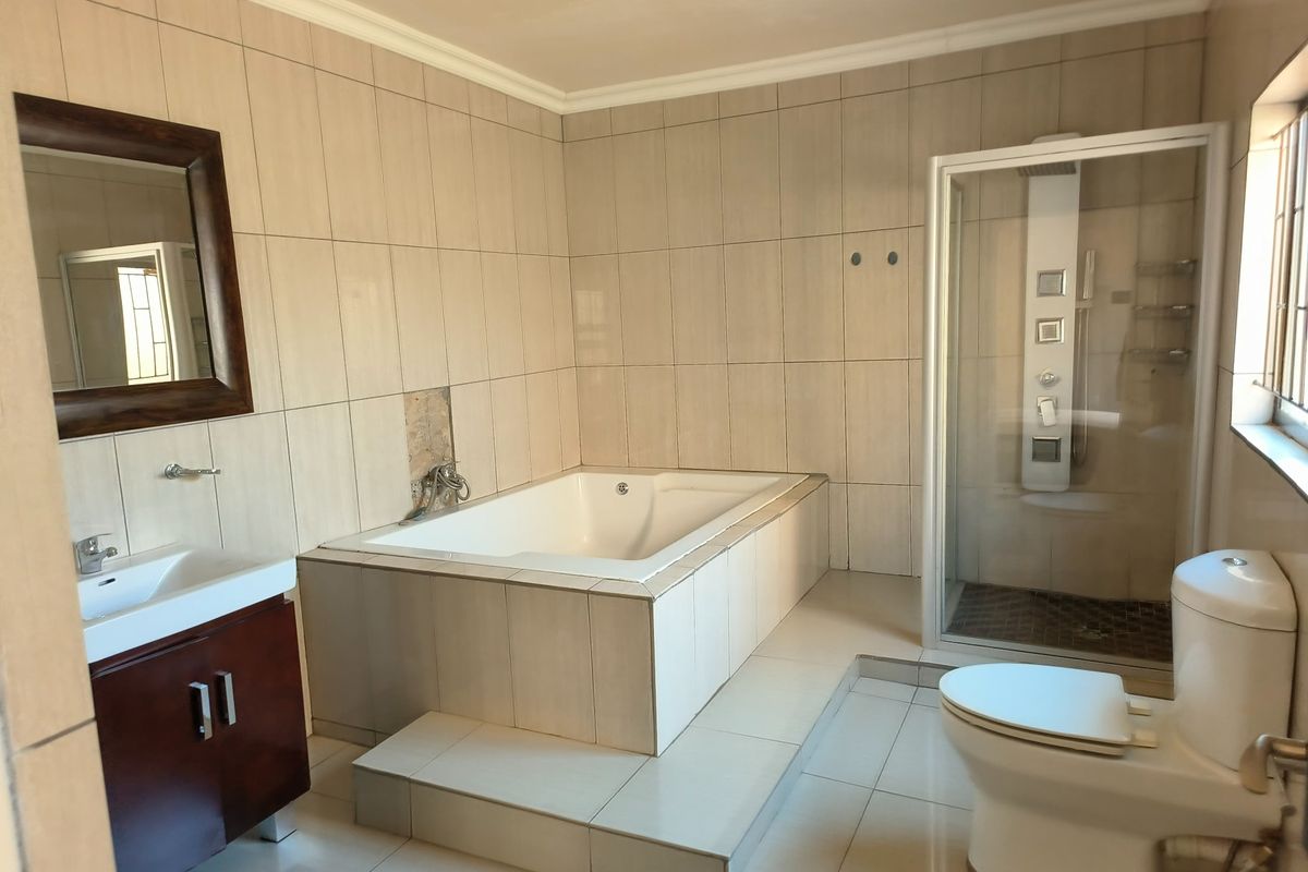 A spacious bathroom featuring a built-in bathtub, separate shower enclosure, vanity cabinet, and toilet, finished with neutral wall and floor tiling.
