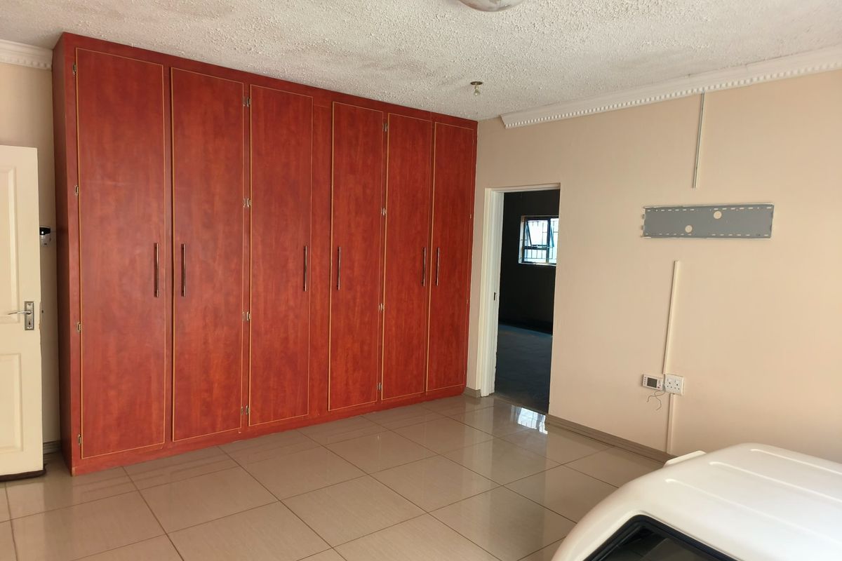 A spacious bedroom featuring extensive built-in wooden cupboards, neutral tiled flooring, and decorative ceiling cornicing.