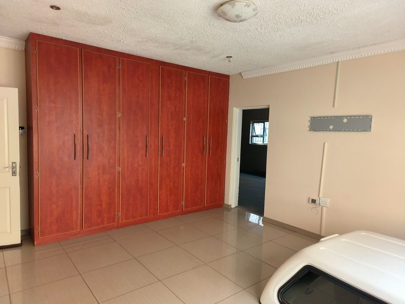 A spacious bedroom featuring extensive built-in wooden cupboards, neutral tiled flooring, and decorative ceiling cornicing.