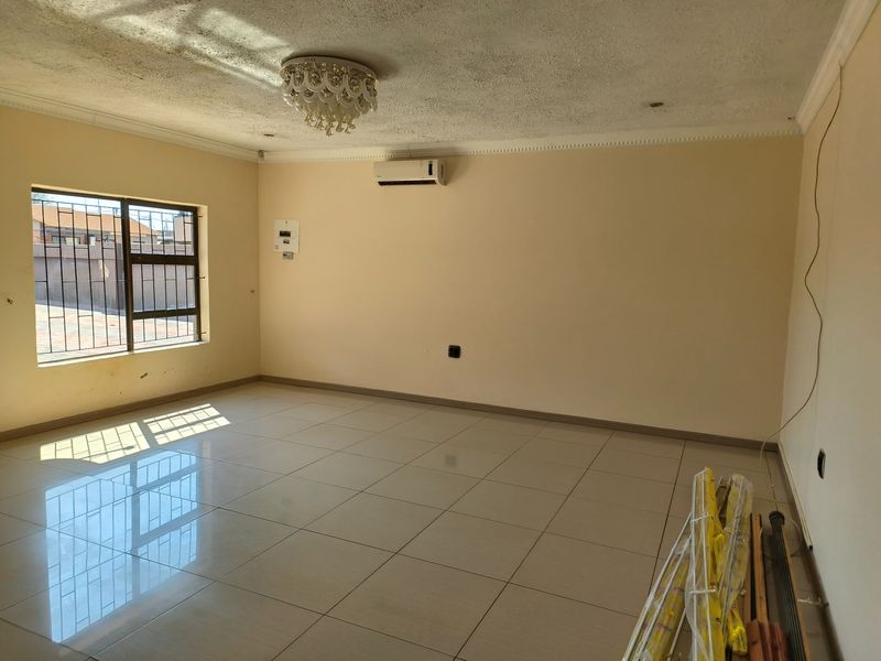 Spacious, empty living area featuring neutral tiled flooring, a wall-mounted air conditioning unit, and security-fitted windows.