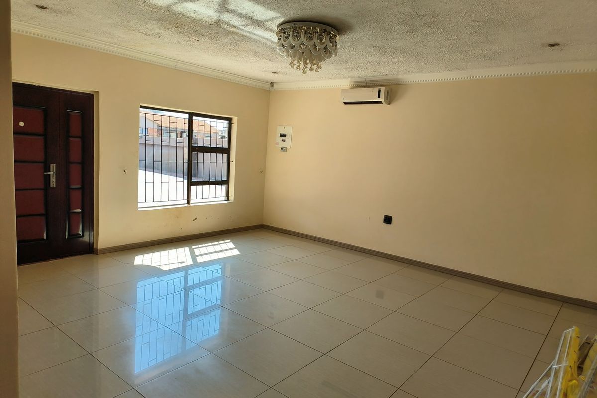 A spacious, empty living area featuring polished tiled floors, an air conditioning unit, and security bars on the windows.