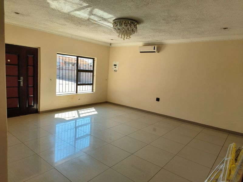 A spacious, empty living area featuring polished tiled floors, an air conditioning unit, and security bars on the windows.