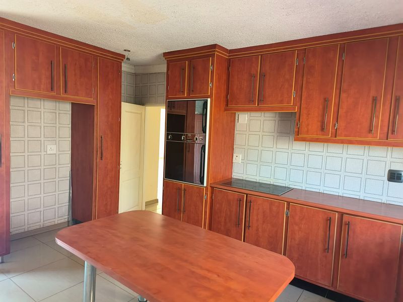 A spacious kitchen featuring dated wood-finish cabinetry, a built-in oven, electric hob, tiled backsplash, and a central island, offering a functional layout for renovation.