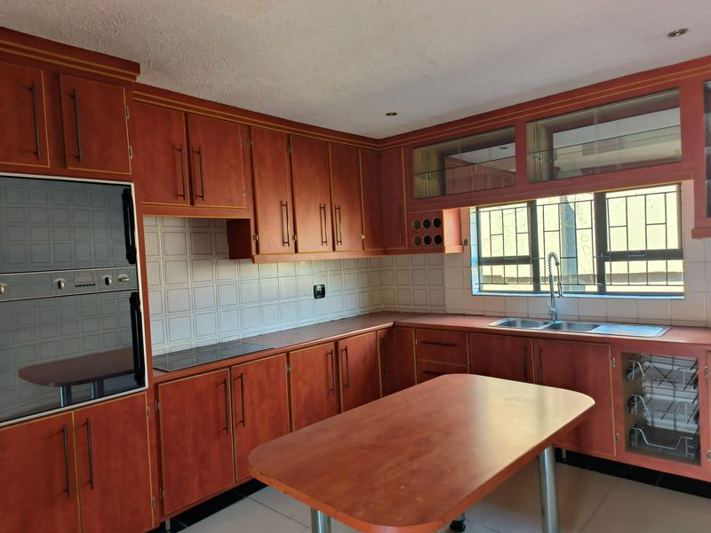 A functional kitchen featuring wood-toned cabinetry, built-in oven, electric hob, and a central island, offering a classic layout with ample storage space.