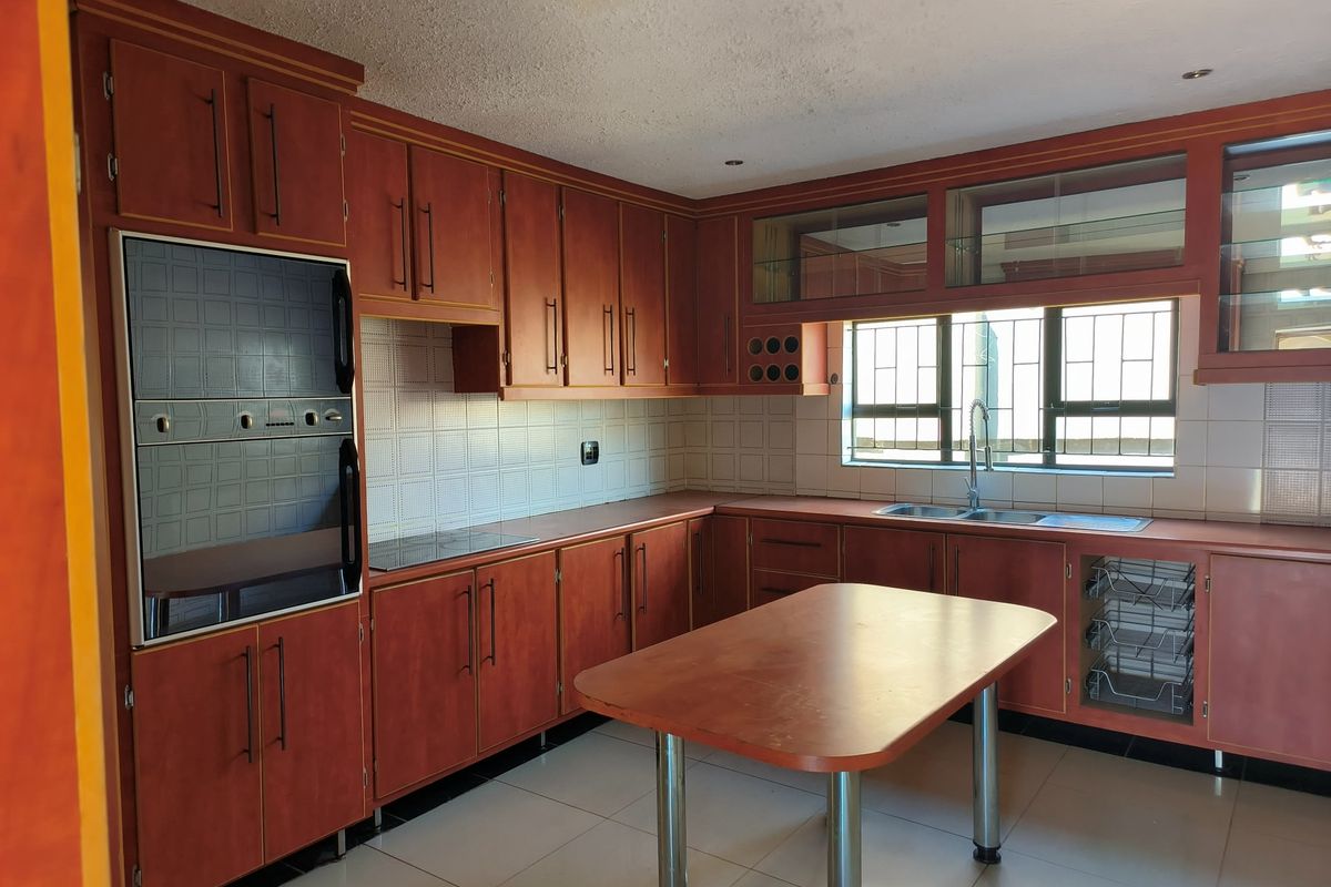 A spacious kitchen featuring extensive wooden cabinetry, a built-in double oven, ceramic hob, and a central island, offering a functional layout with tiled finishes.