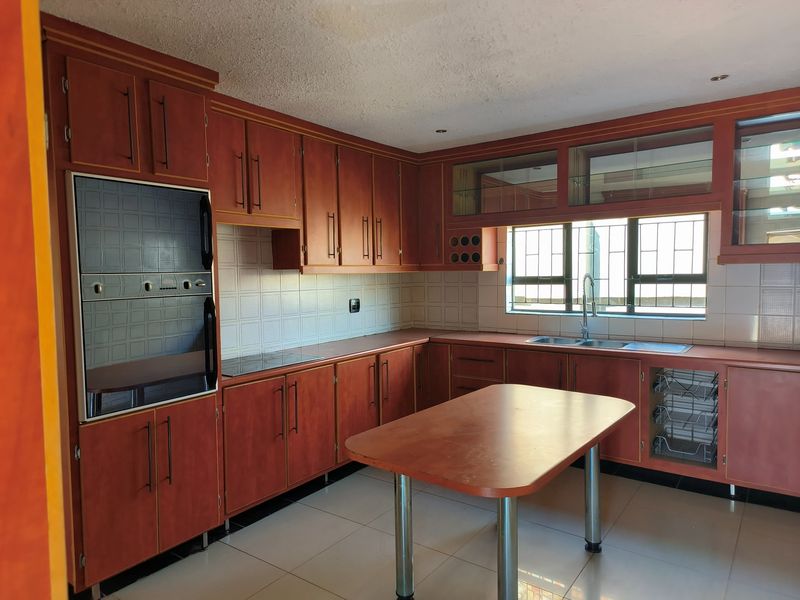 A spacious kitchen featuring extensive wooden cabinetry, a built-in double oven, ceramic hob, and a central island, offering a functional layout with tiled finishes.