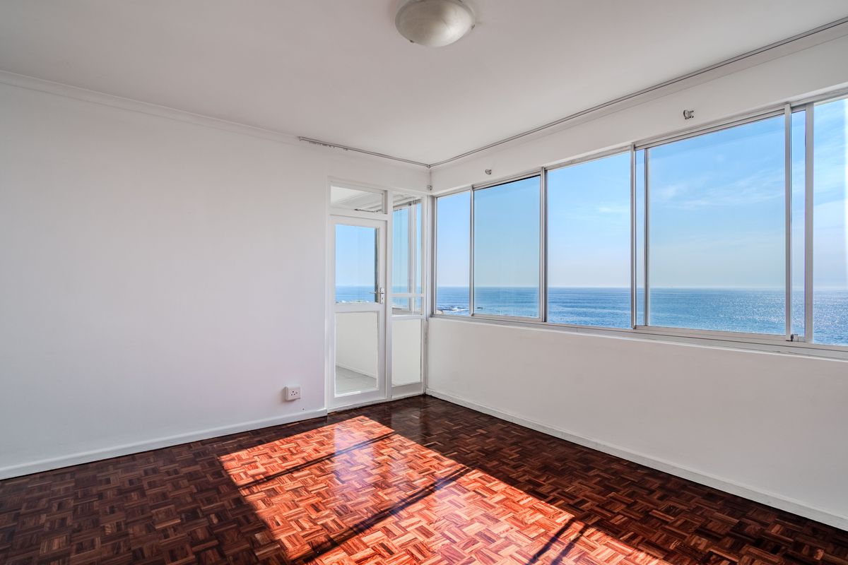 Bright and spacious living area featuring classic parquet flooring, large sliding windows, and direct access to a balcony with expansive ocean views.