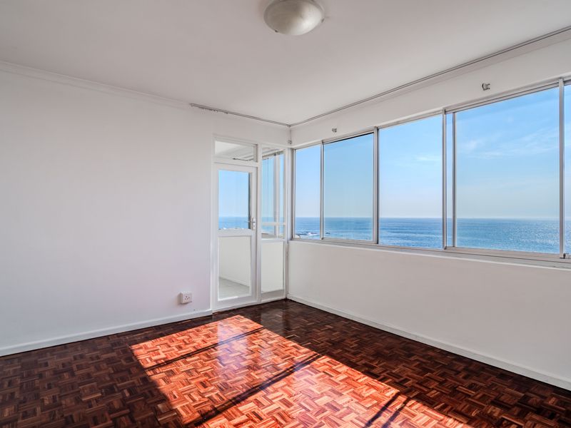 Bright and spacious living area featuring classic parquet flooring, large sliding windows, and direct access to a balcony with expansive ocean views.