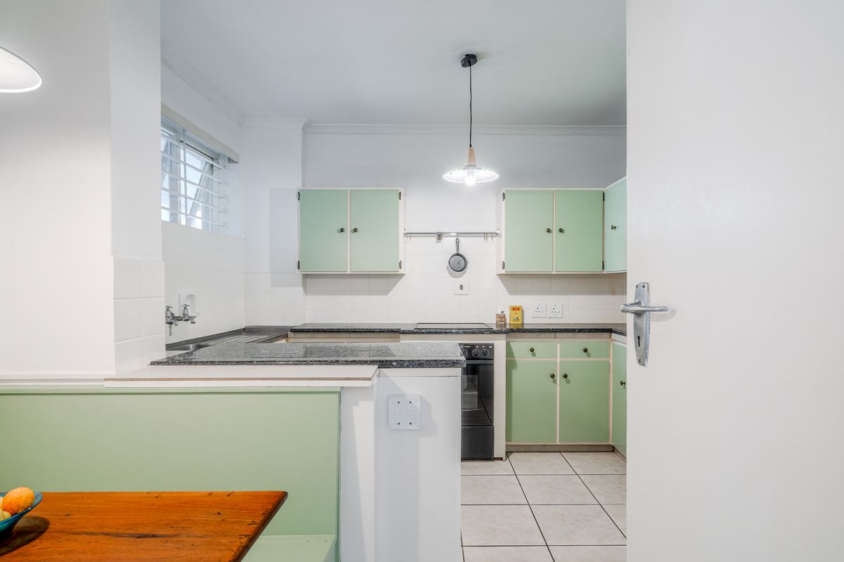 A functional kitchen featuring vintage-style green cabinetry, stone countertops, tiled flooring, and integrated cooking appliances, offering a clean and well-maintained workspace.