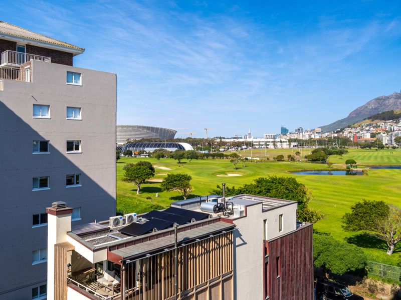 Elevated view overlooking a golf course, stadium, and mountain range, showcasing the surrounding urban landscape and green space.