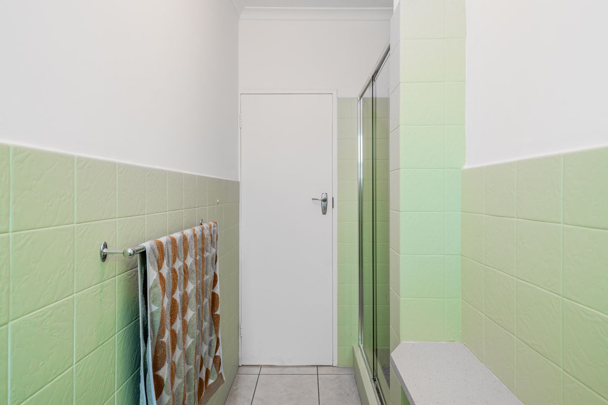 A functional bathroom featuring light green wall tiling, a shower enclosure, and tiled flooring.