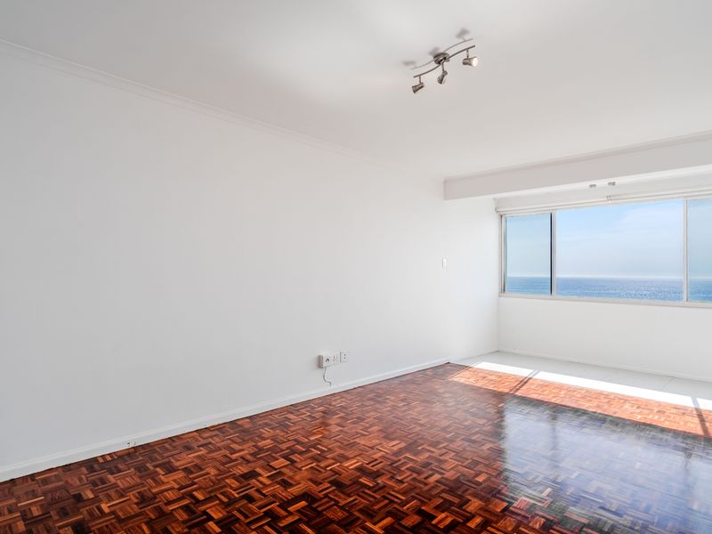 An empty living room featuring polished parquet flooring, a ceiling spotlight fixture, and a large window offering expansive ocean views.