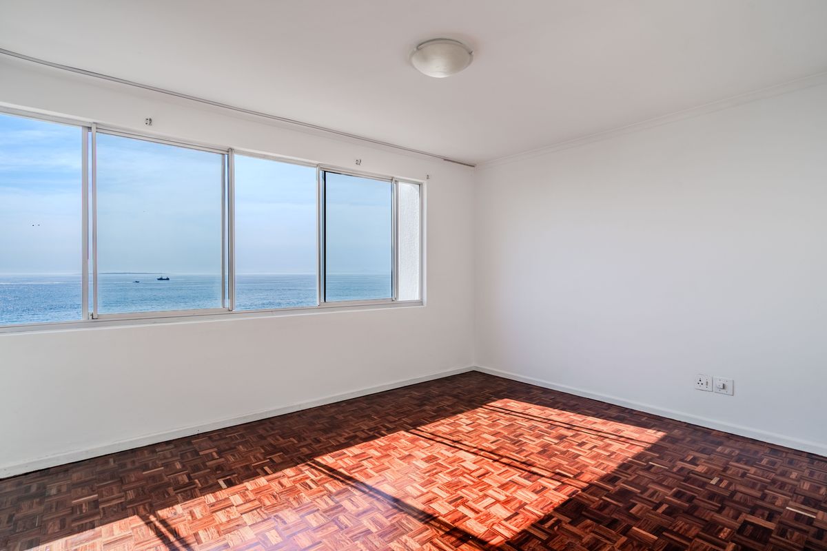 A bright, empty bedroom featuring classic parquet flooring and large sliding windows that offer expansive ocean views.