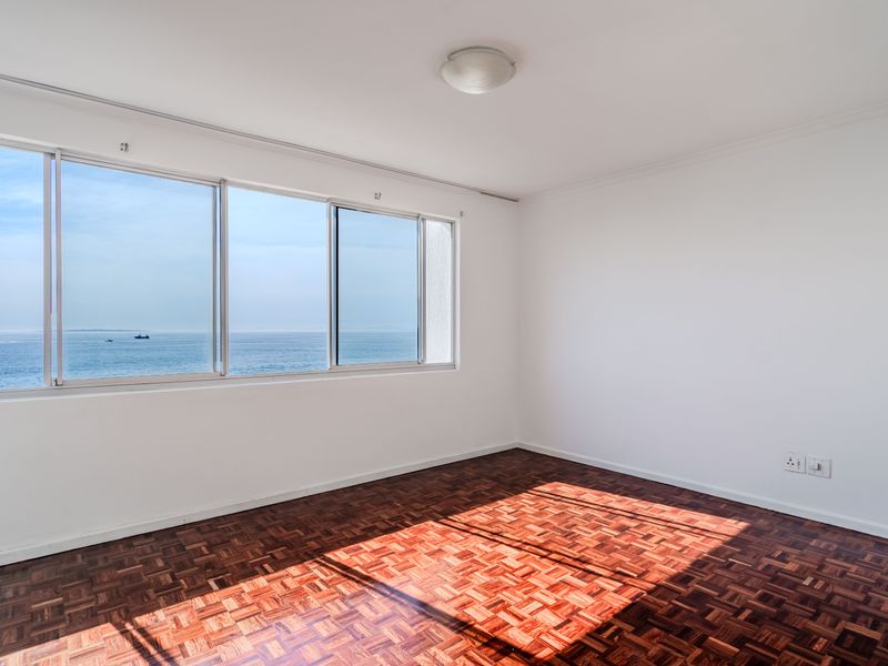 A bright, empty bedroom featuring classic parquet flooring and large sliding windows that offer expansive ocean views.