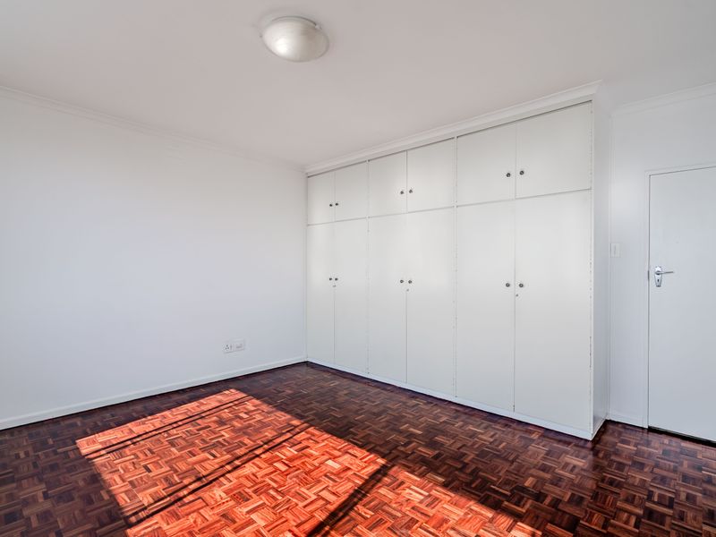 A bright, empty bedroom featuring classic parquet flooring and extensive floor-to-ceiling built-in cupboards for ample storage.