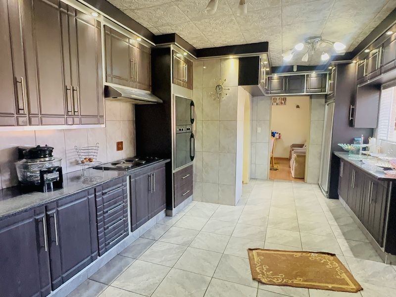 A spacious kitchen featuring dark wood cabinetry, granite countertops, built-in oven, hob, and extractor fan with neutral tiled flooring and backsplash.