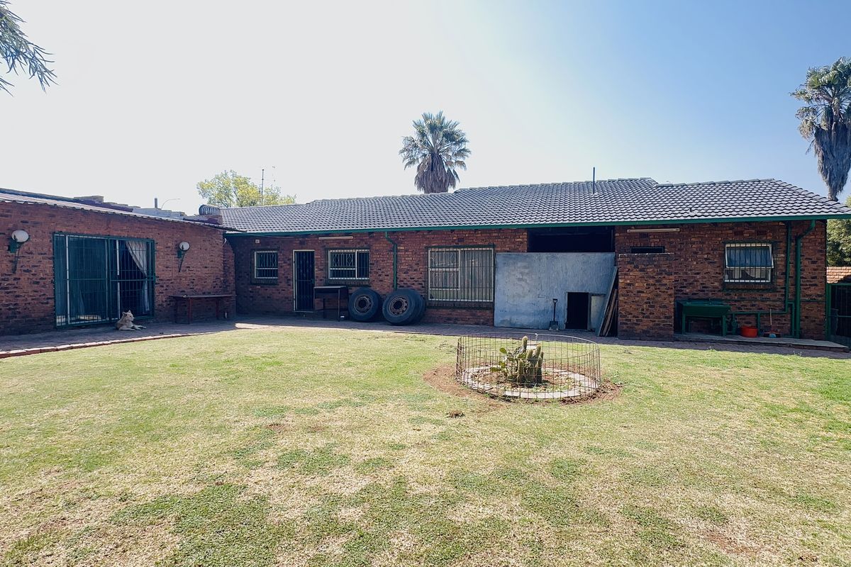 A spacious rear garden featuring a face brick house exterior with a tiled roof, security bars on windows, and a large lawn area.