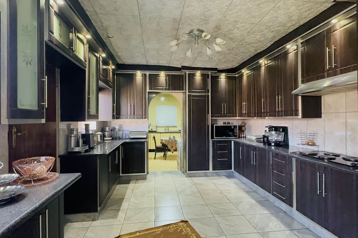 Spacious kitchen featuring dark wood cabinetry, granite countertops, built-in oven, extractor fan, and tiled flooring with integrated lighting.