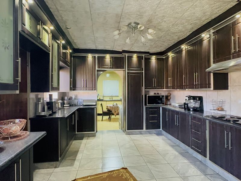 Spacious kitchen featuring dark wood cabinetry, granite countertops, built-in oven, extractor fan, and tiled flooring with integrated lighting.