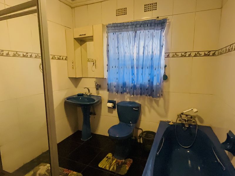 A dated bathroom featuring a blue pedestal basin, toilet, and bathtub, complemented by a separate shower enclosure and tiled wall finishes.