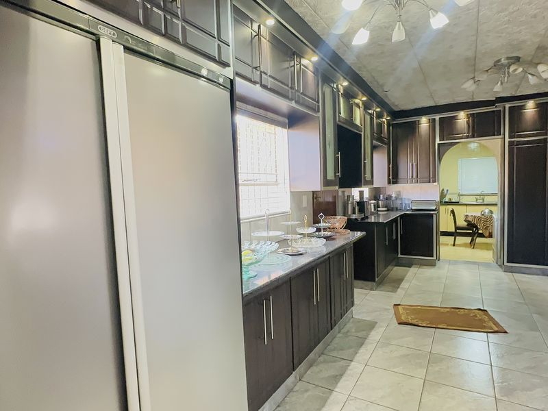 Spacious kitchen featuring dark wood cabinetry, granite countertops, tiled flooring, and integrated appliances with a seamless flow into the adjacent dining area.