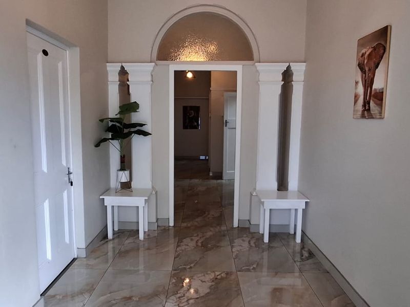 A bright and welcoming entrance hall featuring polished tiled flooring, decorative pillars, and an arched transom window above the doorway.