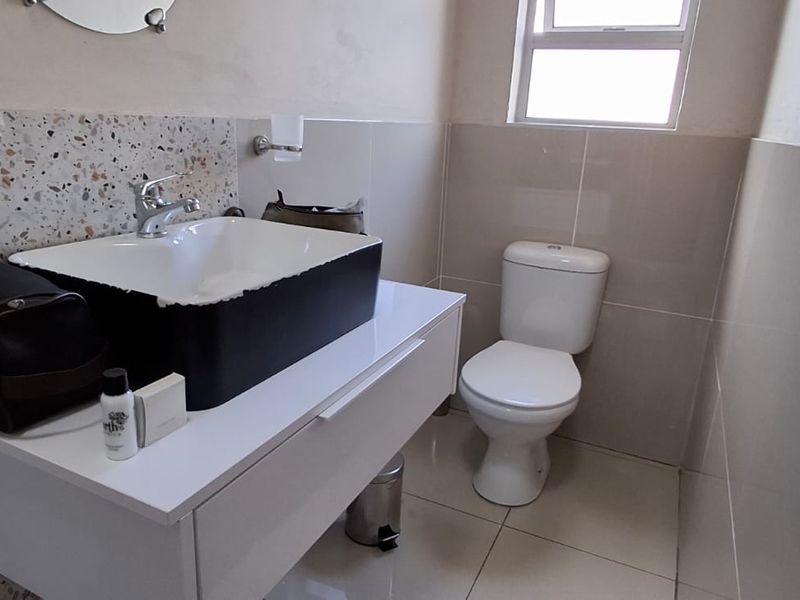 A compact bathroom featuring a modern white vanity with a vessel sink, a toilet, and neutral wall and floor tiling.