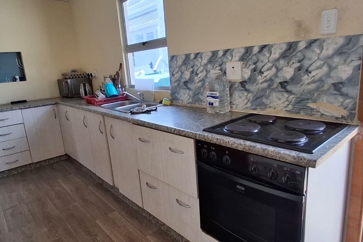 A functional kitchen featuring laminate cabinetry, a built-in electric stove, and a tiled backsplash, showing signs of wear and requiring cosmetic updates.
