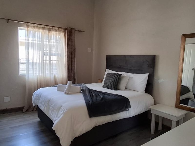 A functional guest bedroom featuring laminate flooring, neutral wall finishes, and a window with curtain treatments.
