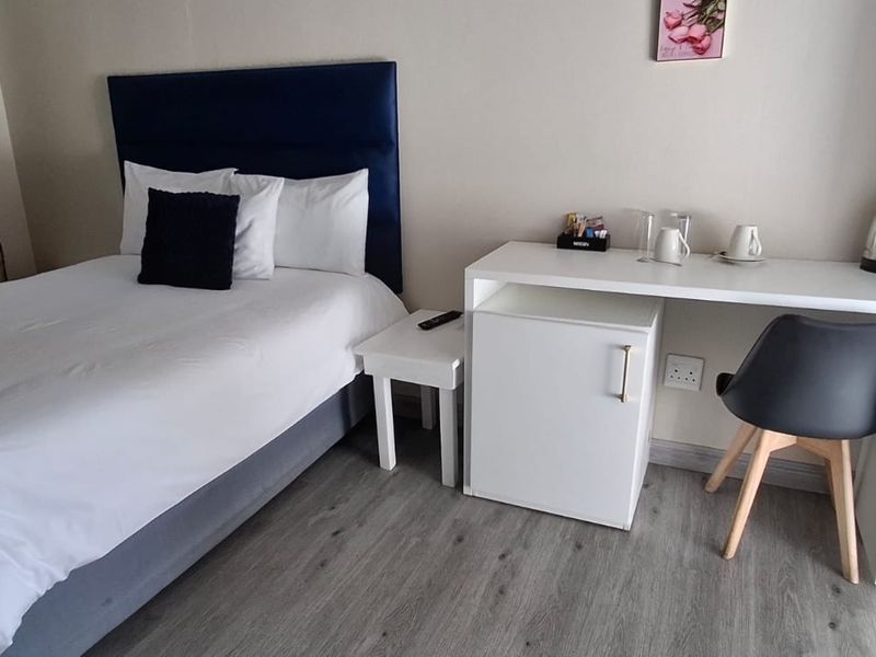 A clean and functional guest bedroom featuring modern laminate flooring and neutral wall finishes.