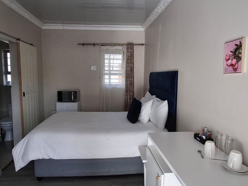 A functional bedroom featuring a sliding door leading to an en-suite bathroom, neutral wall finishes, and a window with security bars.