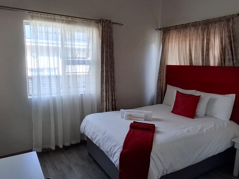 A compact bedroom featuring laminate flooring, neutral walls, and dual windows with curtain rods, providing a functional space for guests.