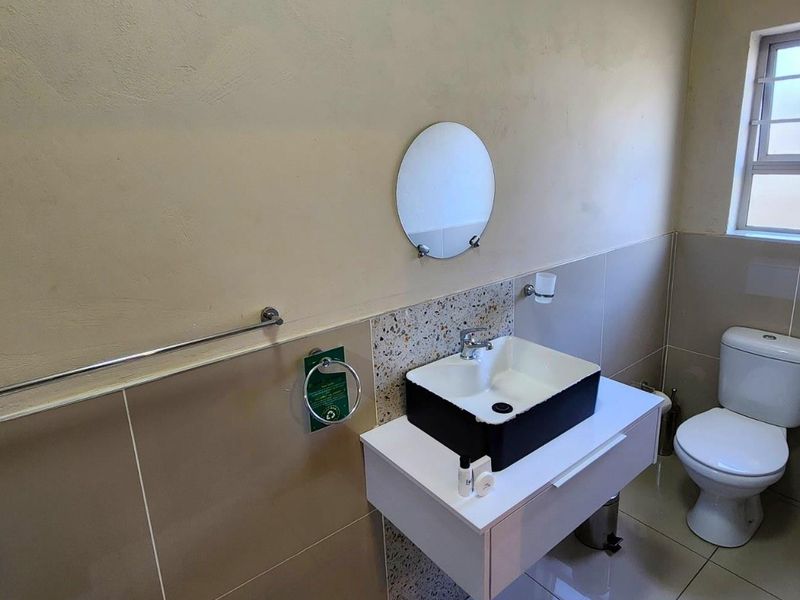 A modern bathroom featuring a vessel sink on a vanity cabinet, a toilet, and neutral wall and floor tiling.