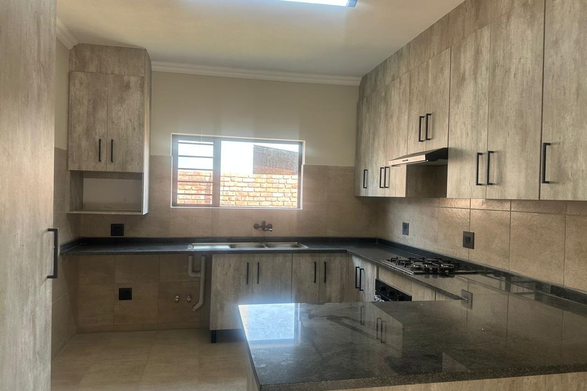 A modern, empty kitchen featuring wood-look cabinetry, dark stone countertops, a gas hob, extractor fan, and tiled backsplash.
