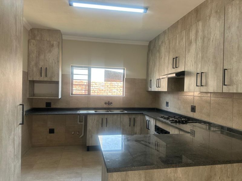 A modern, empty kitchen featuring wood-look cabinetry, dark stone countertops, a gas hob, extractor fan, and tiled backsplash.