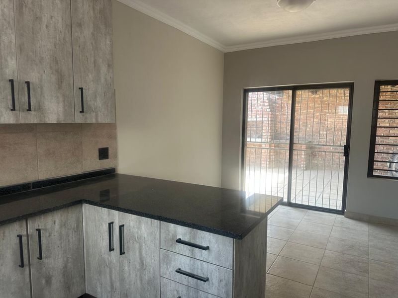 Modern kitchen featuring grey laminate cabinetry, dark granite countertops, and tiled flooring, with direct access to an outdoor patio area through sliding glass doors.