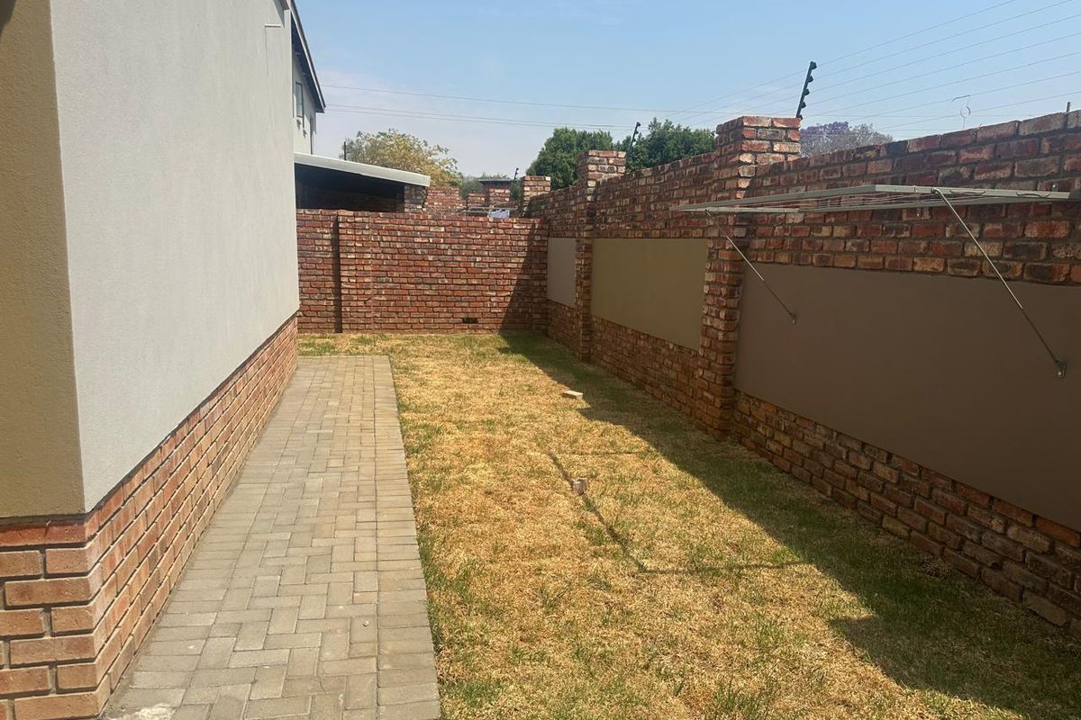 A private rear garden area featuring a paved walkway, brick boundary walls with electric fencing, and a wall-mounted drying rack.