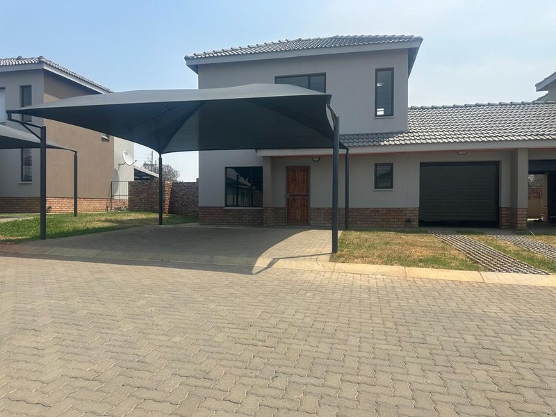 Front elevation of a modern townhouse featuring a paved driveway, a large shadeport, a single garage, and a timber entrance door.