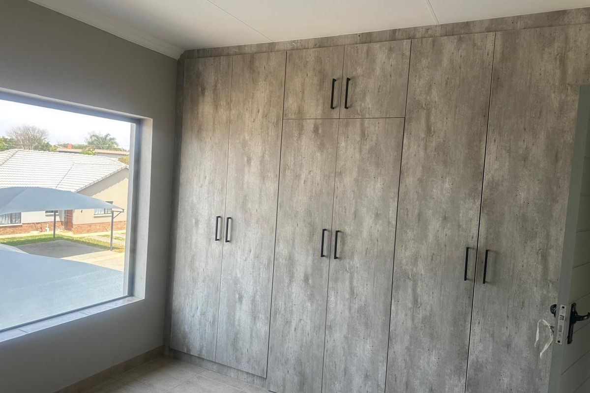 A bright bedroom featuring modern, wood-look built-in cupboards and neutral tiled flooring, offering a clean and contemporary aesthetic.