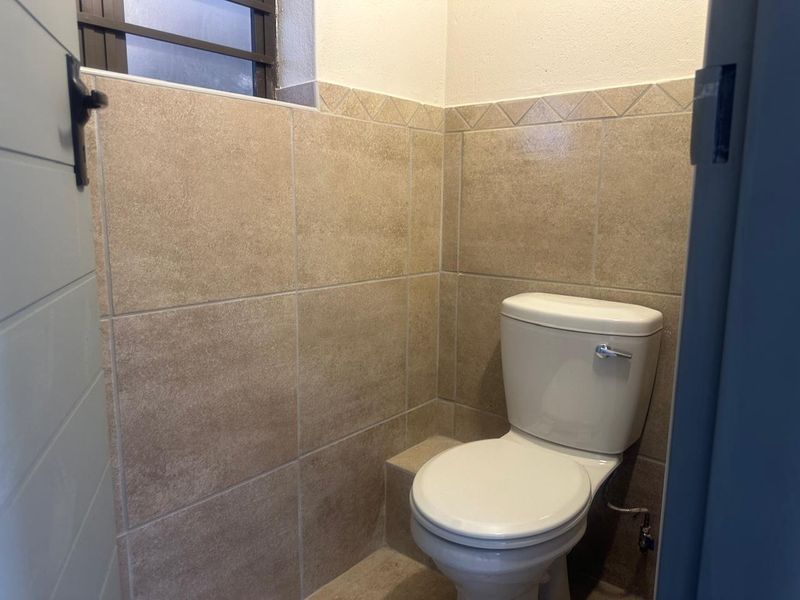 A compact bathroom featuring neutral ceramic wall tiles and a standard toilet, providing a functional and clean space.