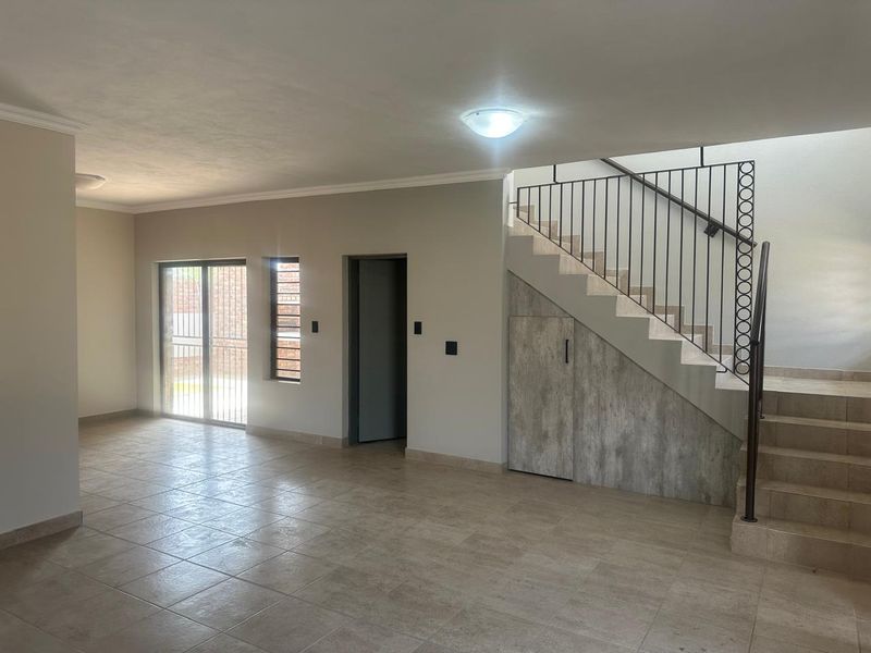 Spacious, empty living area featuring neutral tiled flooring, a modern under-stair storage unit, and access to the exterior via a sliding glass door.